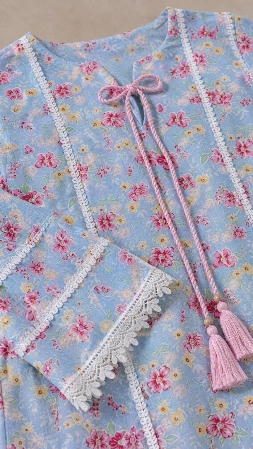 Close-up of light blue floral fabric, lace trim, and pink tassel tie details