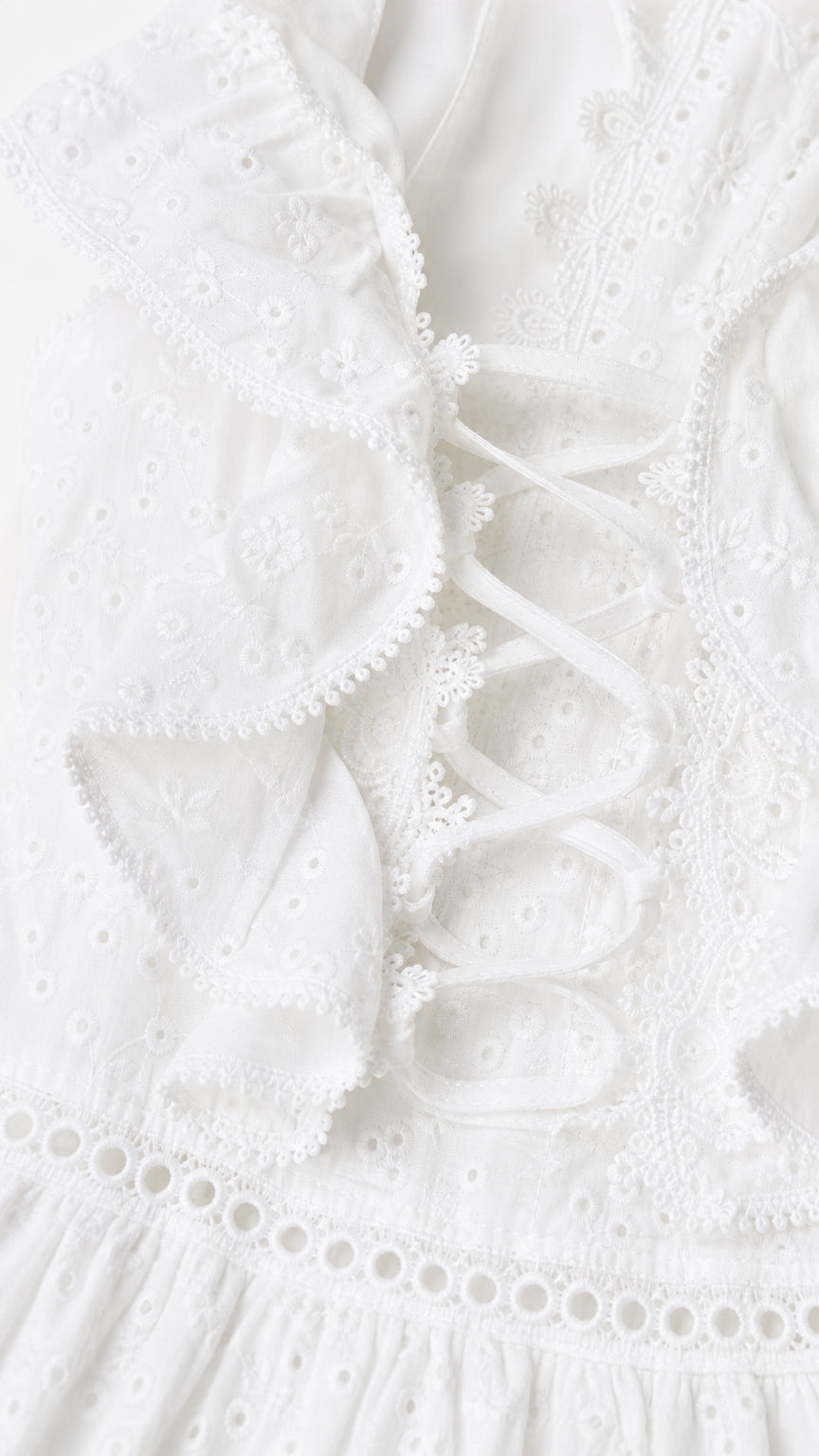 Close-up detail of white eyelet embroidery, ruffle trim, and side lace-up ties